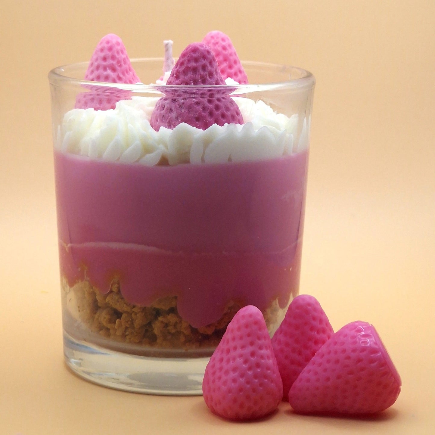 Glass dessert with pink and white layers, topped with pink strawberry-shaped candies on a beige background.