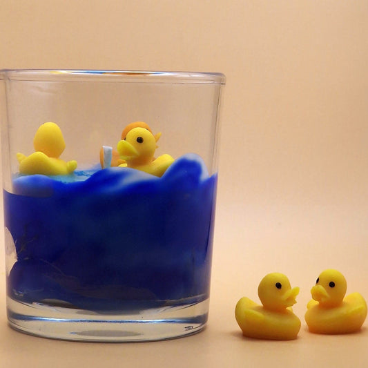 Glass with blue wax and yellow rubber ducks on a beige background