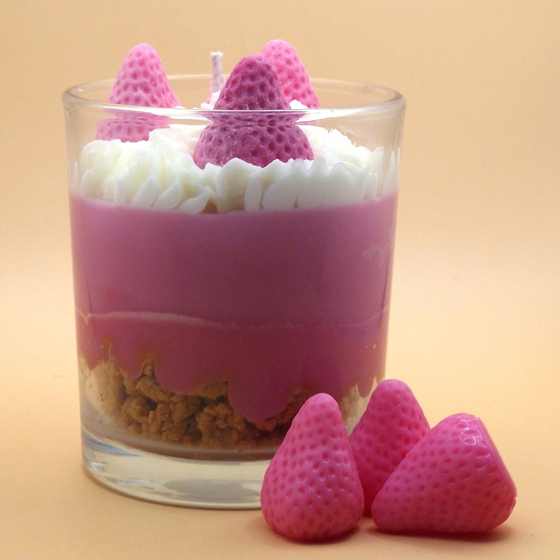 Glass dessert with pink and white layers, topped with pink strawberry-shaped candies on a beige background.