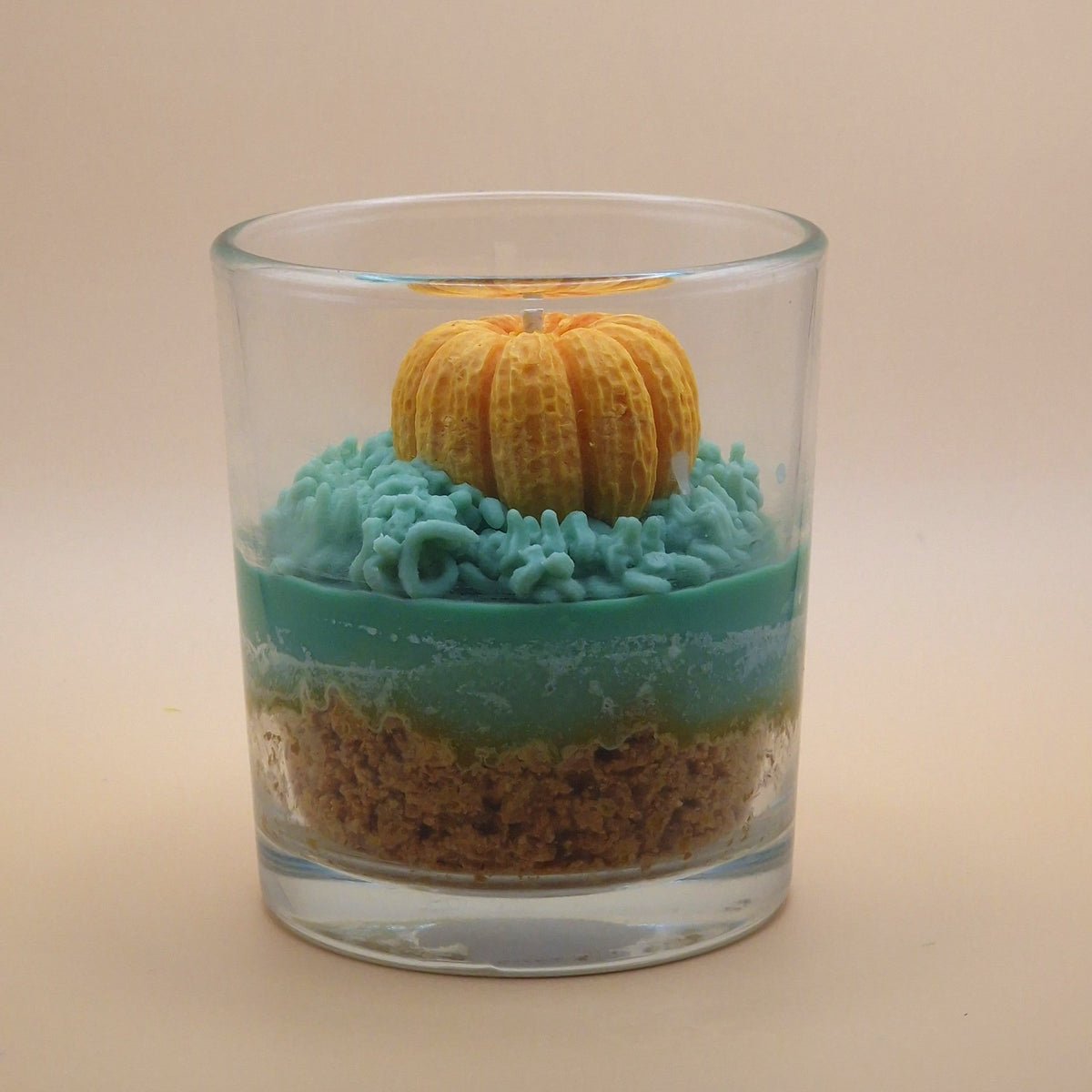 Detail van Warme Herfst geurkaars: oranje pompoen met lont op groene waskrullen in een glazen pot.