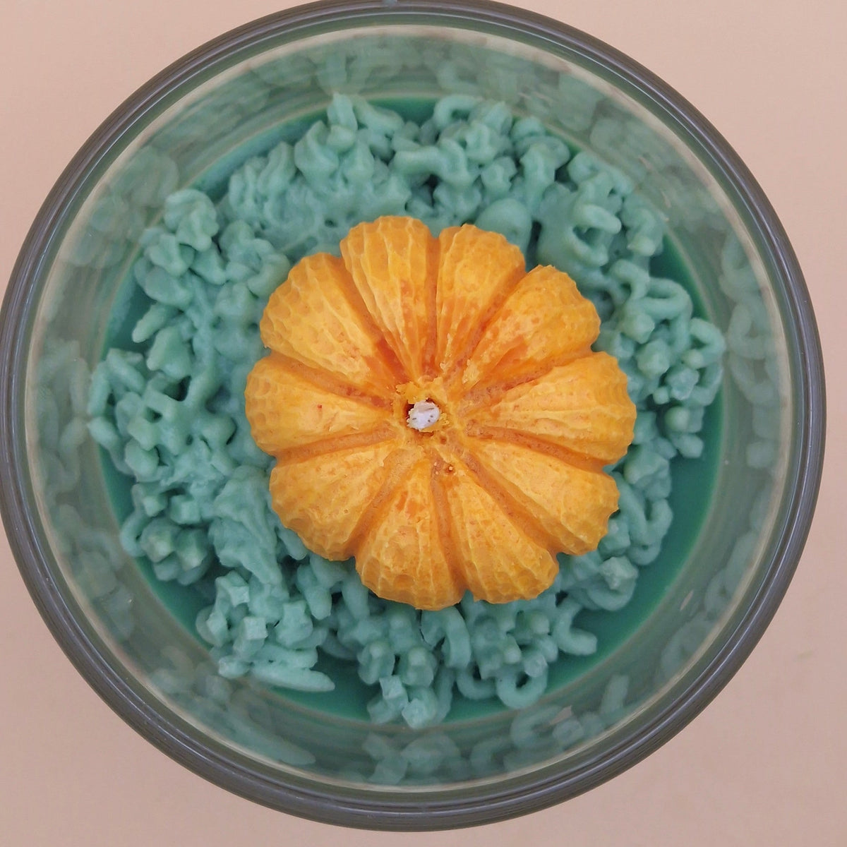 Detail van Warme Herfst geurkaars: oranje pompoen met lont op groene waskrullen in een glazen pot.