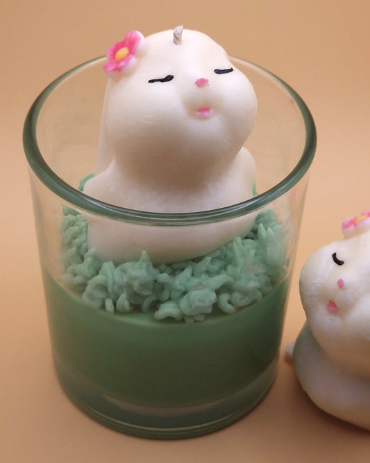 Cute animal-shaped candle with a flower on top inside a glass container on a beige background