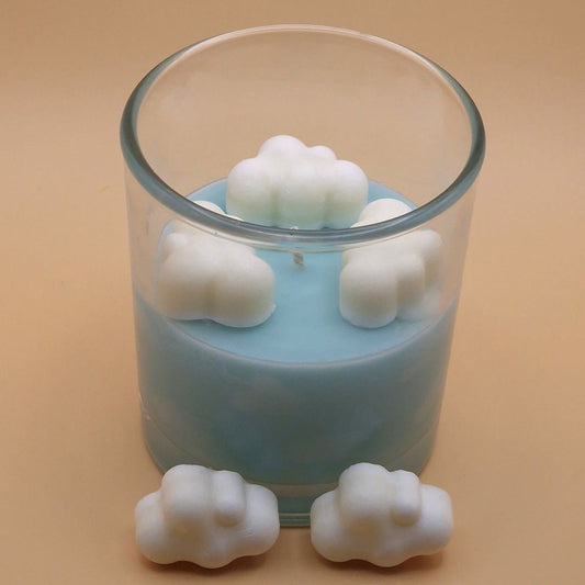 Candle in a glass jar with cloud-shaped wax pieces on a beige background