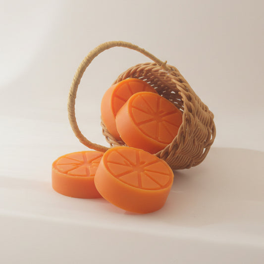 Oranje Spiced Orange wax melts in de vorm van sinaasappelschijfjes in en naast een rieten mandje.
