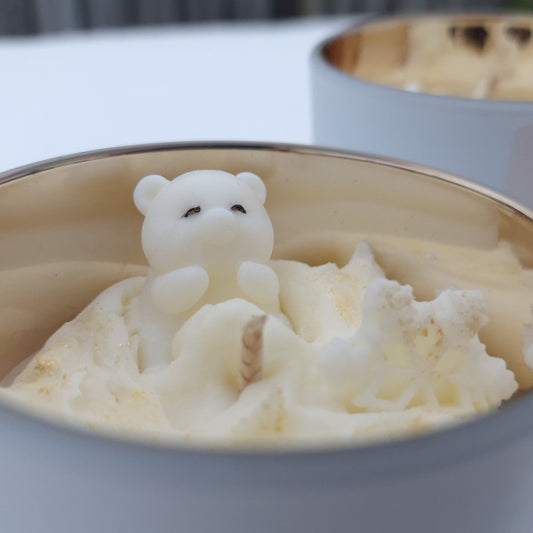 Handgemaakte Snow Bear geurkaars van sojawas met gouden binnenkant, geplaatst in sneeuw.