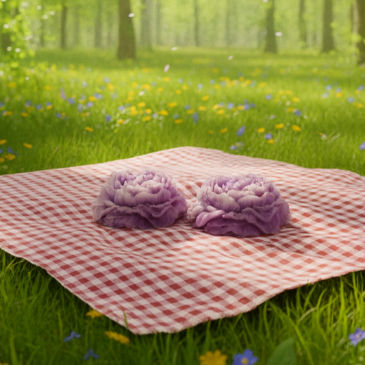 Pink checkered blanket with purple flowers on a grassy field in a forest