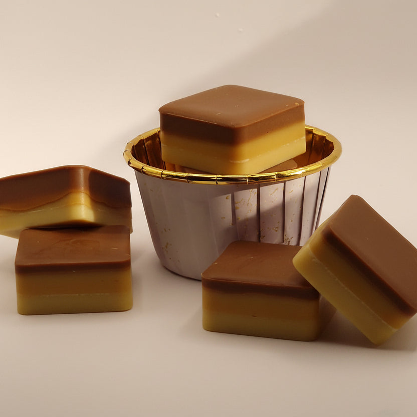 Vierkante Millionaire’s Shortbread wax melts met gele en bruine lagen in en naast een mandje.