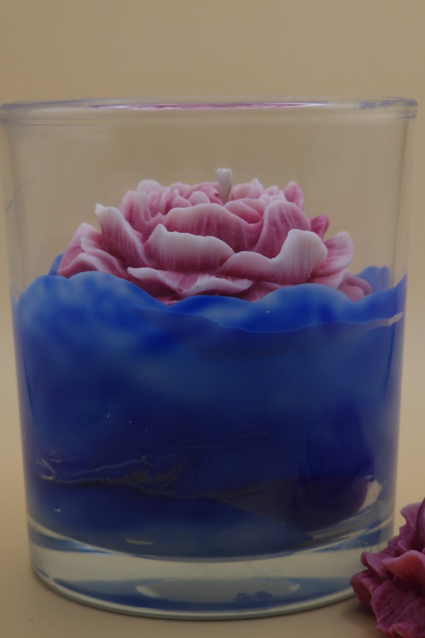 Glass candle holder with pink rose and blue wax on a beige background