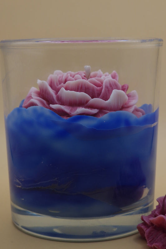 Glass candle holder with pink rose and blue wax on a beige background